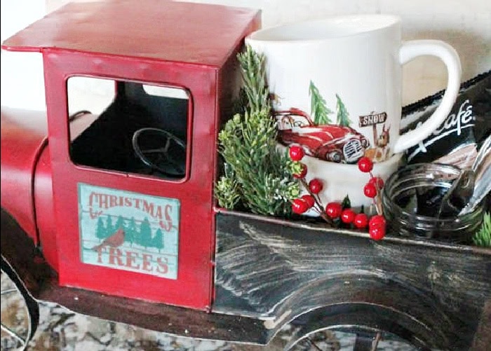 Red truck Christmas coffee bar filled with a mug, spoons, coffee pods, and greenery.