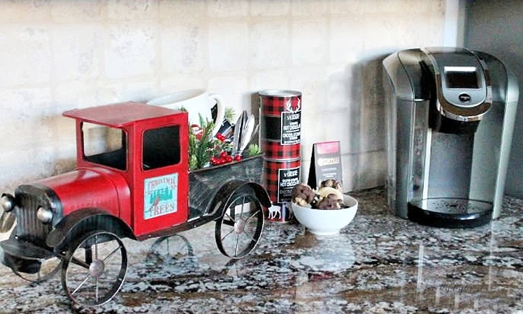 Red truck Christmas coffee station beside a Keurig with hot chocolate and coffee supplies.