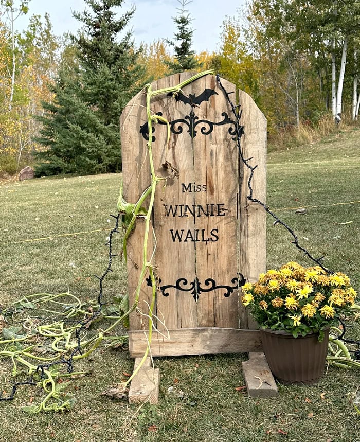 Rustic Halloween pallet gravestone with black scrollwork, trailing vines and yellow flowers.