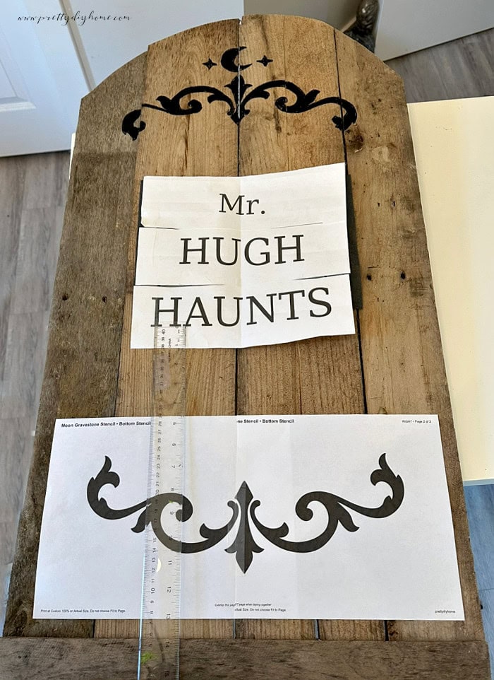 Positioning printable lettering and decorative stencils on a pallet wood Halloween gravestone.