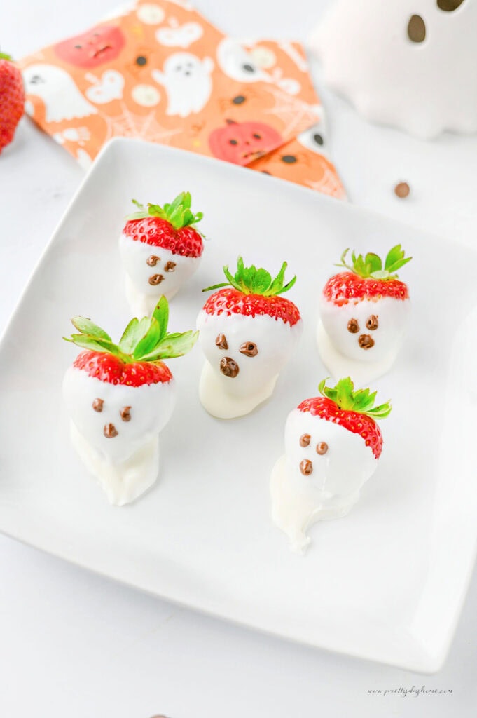 Cute strawberry ghosts dipped in white chocolate with simple chocolate faces for Halloween.
