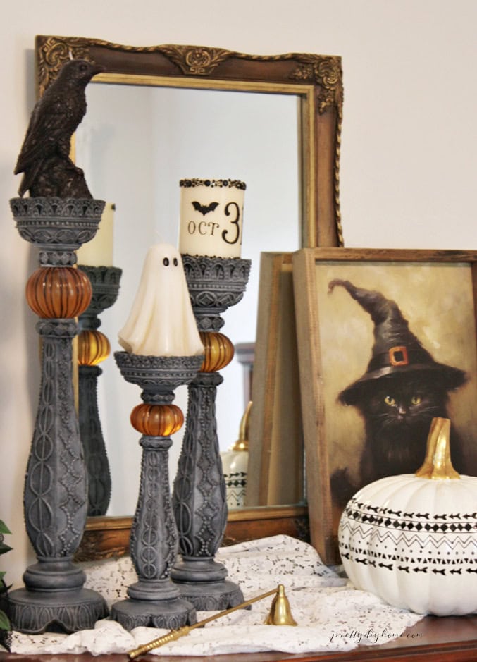 Vintage Halloween candlesticks styled with a ghost candle, black crow candle, OCT 31 pillar candle, pumpkin, and antique mirror.