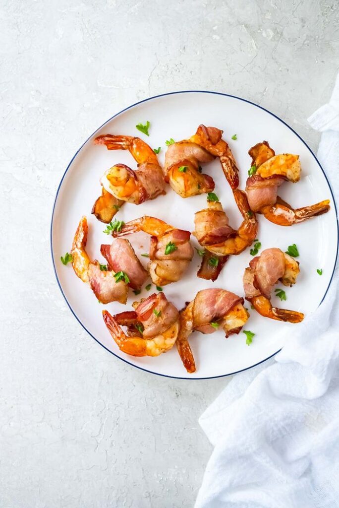 Air fryer bacon-wrapped shrimp cooked until golden, garnished with fresh parsley, and arranged on a white serving plate.