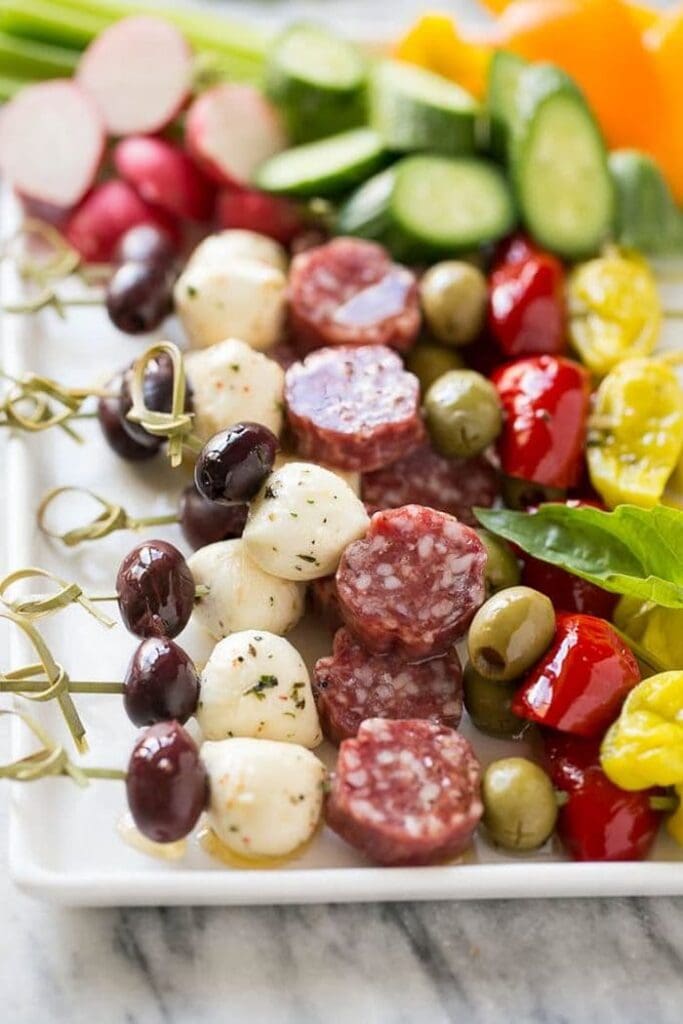 Antipasto skewers threaded with Italian meats, mozzarella cheese, olives, and cherry tomatoes, arranged on a serving platter.