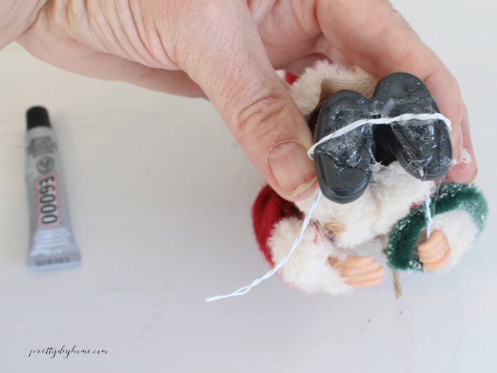 Attaching twisted floral wire to a miniature vintage Santa Claus to create a stem for a DIY Christmas flour sifter arrangement.