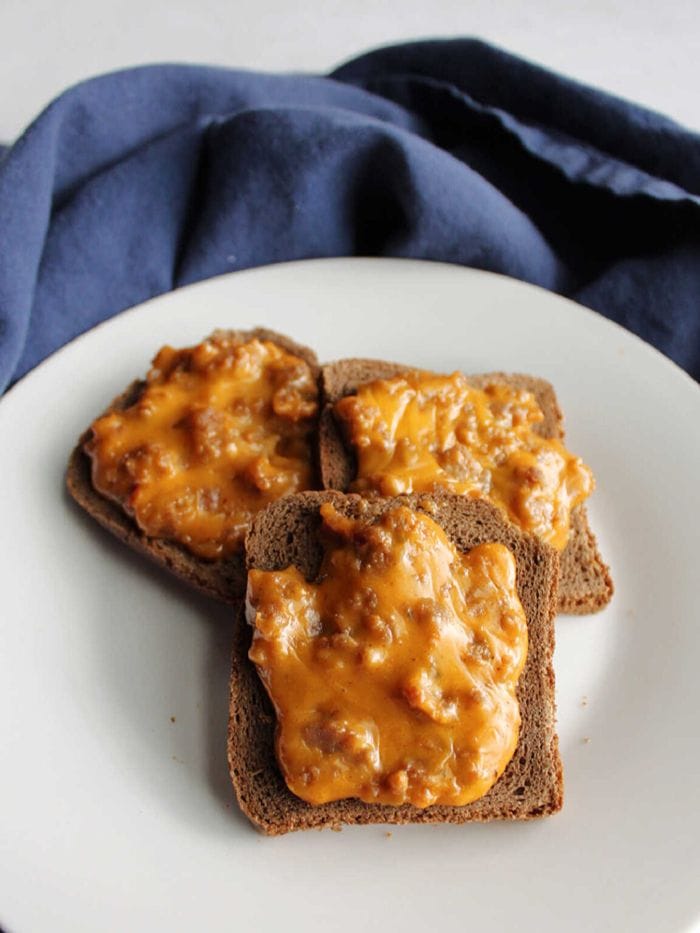 Cheesy party rye appetizers topped with a savoury sausage and melted cheese mixture, served on small slices of rye bread.