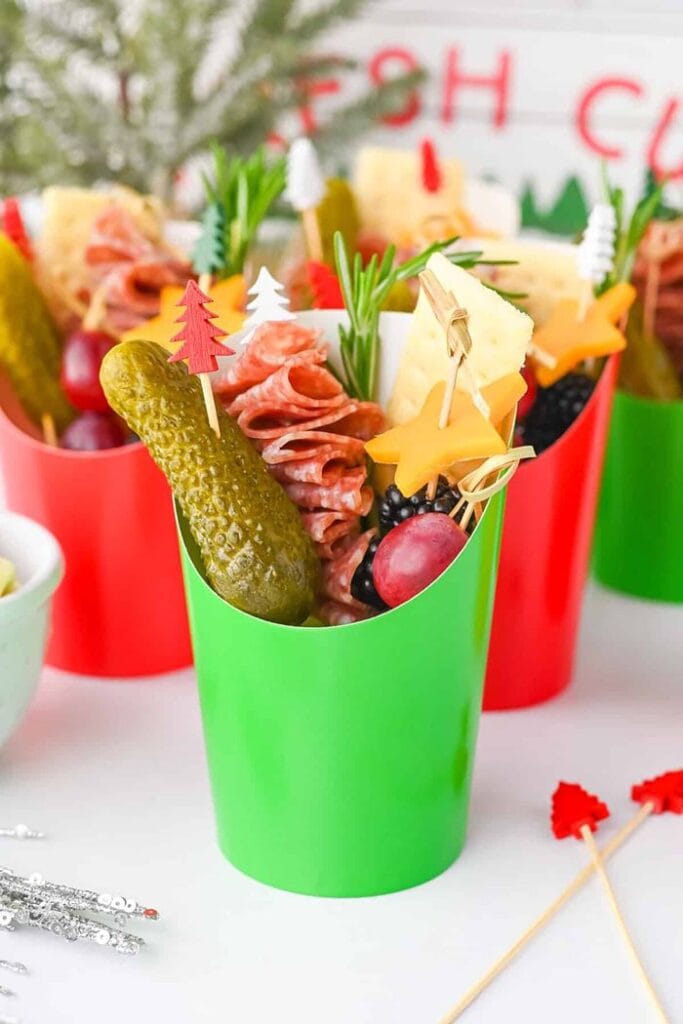 Individual Christmas charcuterie snack cups filled with salami, cheese, pickles, grapes, berries, and festive appetizer skewers.