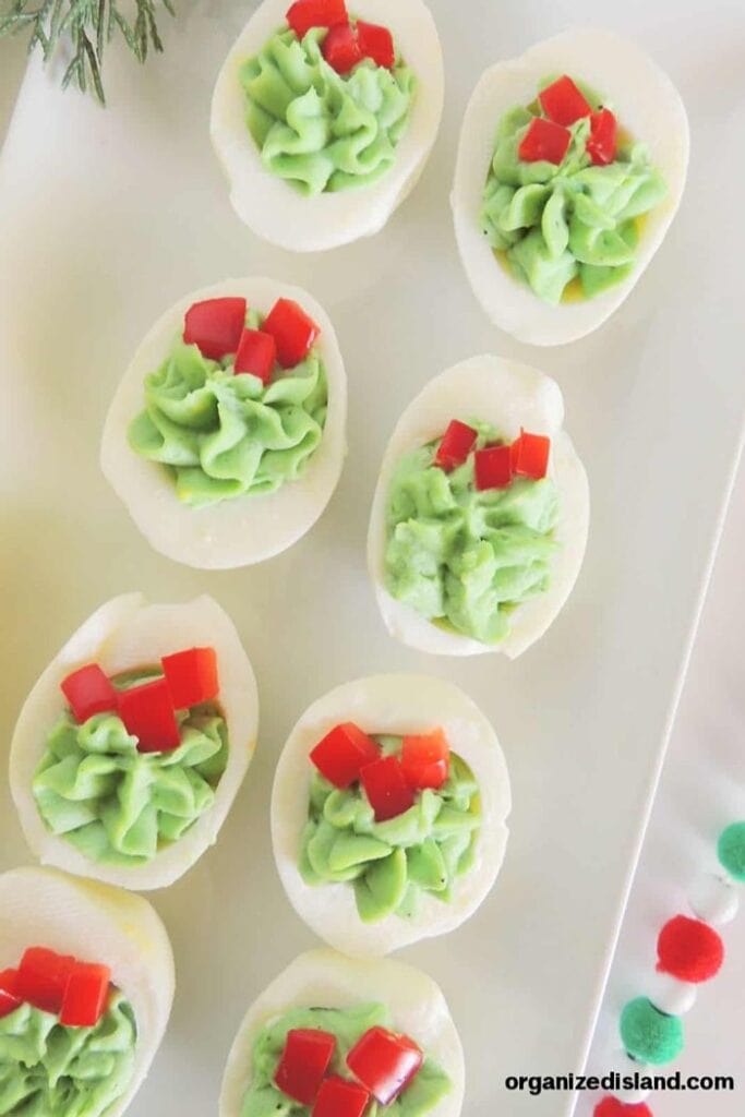 Christmas deviled eggs filled with green piped filling and topped with diced red bell peppers for a festive holiday appetizer.