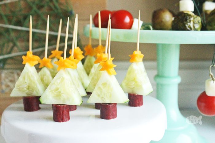 Mini Christmas tree appetizers made with cucumber triangles, cheddar cheese stars, and beef stick trunks, assembled on toothpicks.