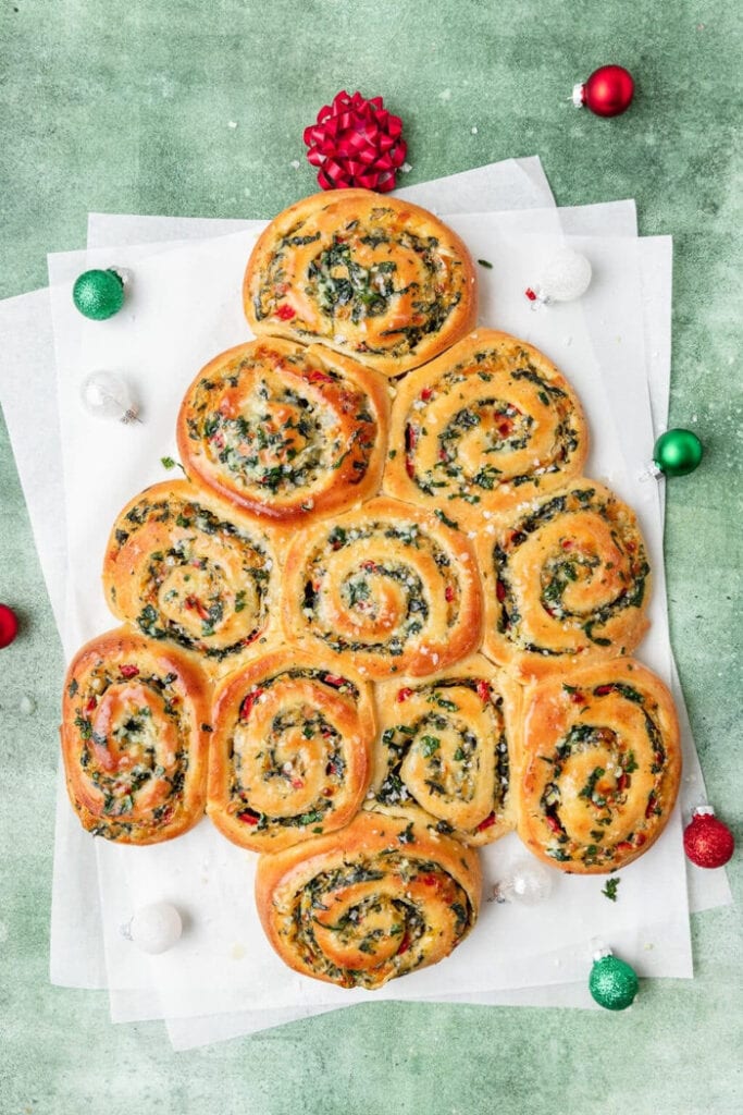 Golden savoury pinwheel rolls with a cheesy herb filling, arranged in the shape of a Christmas tree for a festive holiday appetizer.