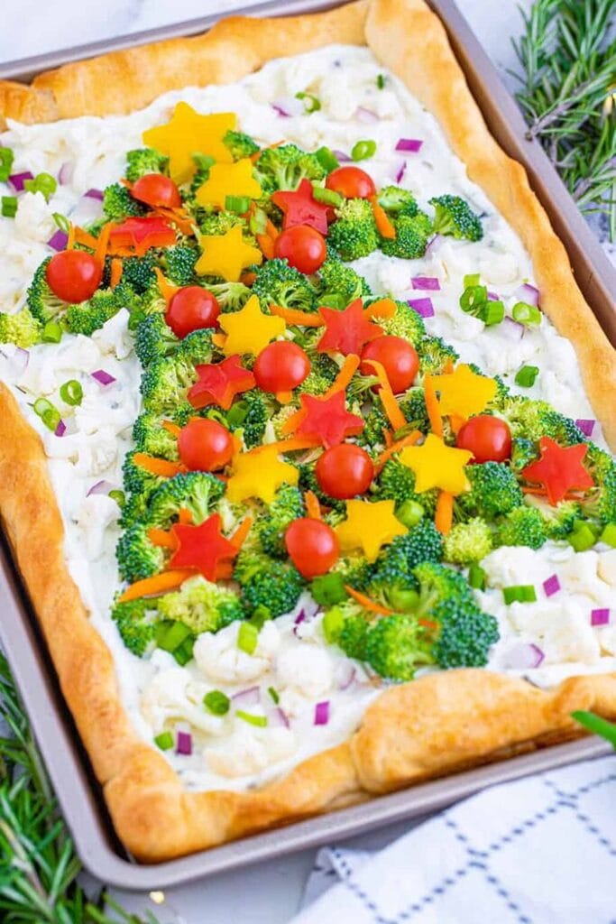 Christmas tree veggie pizza topped with broccoli, cherry tomatoes, colourful bell pepper stars, and a creamy cheese spread on a golden pastry crust.