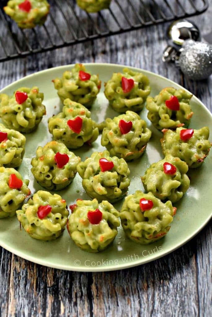 Green Grinch mac and cheese bites decorated with little red bell pepper hearts and arranged on a serving platter.