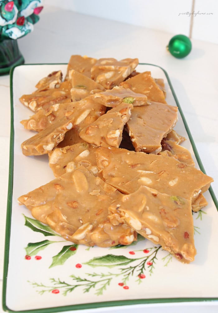 Close-up of homemade peanut brittle with mixed nuts, showing golden crunchy pieces filled with peanuts, cashews, almonds, and pistachios on a vintage holly platter.
