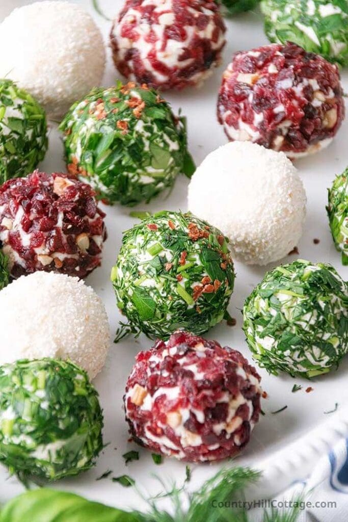 Mini cheese balls rolled in different coatings, including herbs, coconut, and dried cranberries, arranged on a white serving platter.