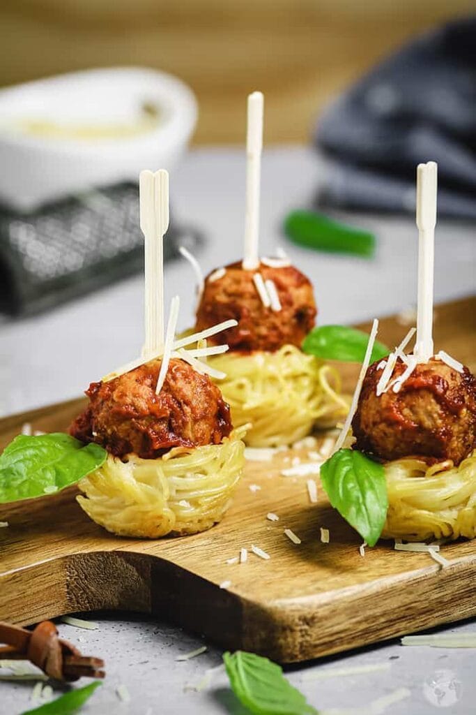 Mini spaghetti nests topped with Italian meatballs, Parmesan cheese, and fresh basil, served with individual appetizer picks.