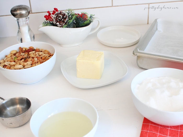 Ingredients for homemade mixed nut peanut brittle, including butter, sugar, corn syrup, assorted nuts, and a parchment-lined baking sheet.