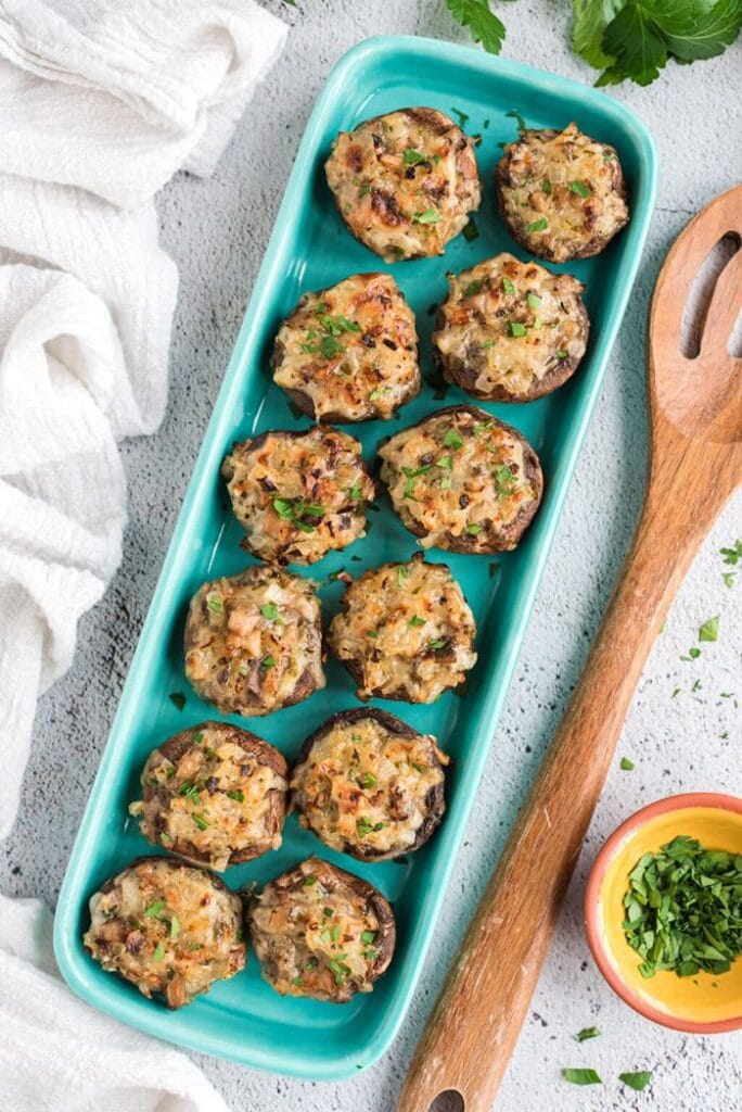 Baked mushrooms filled with mozzarella, Parmesan cheese, onions, and herbs, garnished with fresh parsley on a turquoise serving dish.