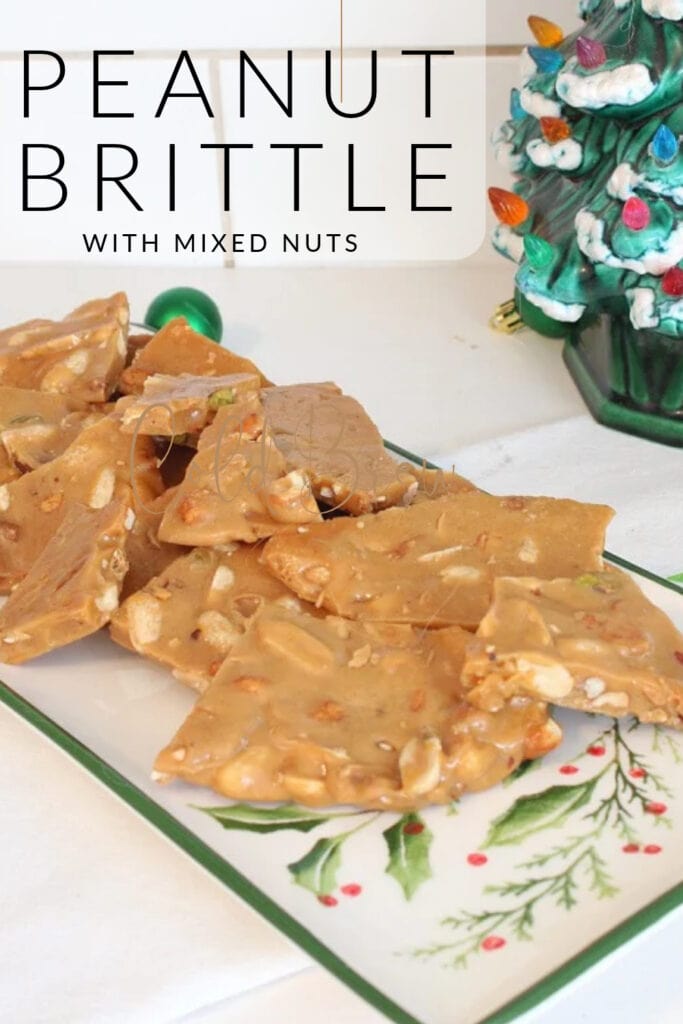 Homemade peanut brittle with mixed nuts on a vintage Christmas platter beside a ceramic Christmas tree.