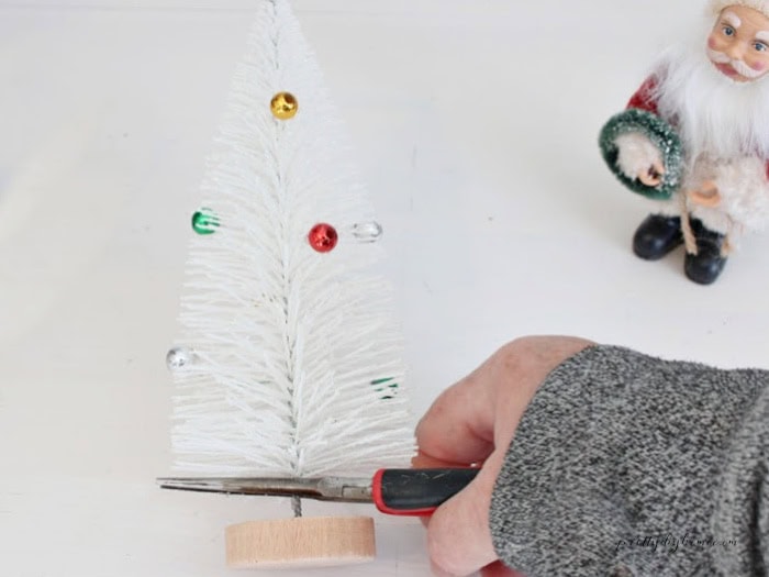 Removing the wooden base from a white bottle brush Christmas tree using needle-nose pliers for a DIY vintage flour sifter Christmas arrangement.