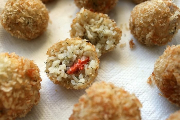 Golden, crispy smoked salmon and caper arancini, with one rice ball cut open to reveal the creamy risotto and smoked salmon filling.