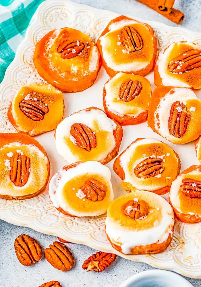 Baked sweet potato rounds topped with toasted marshmallows, pecan halves, and a light sprinkling of sea salt on a white serving platter.