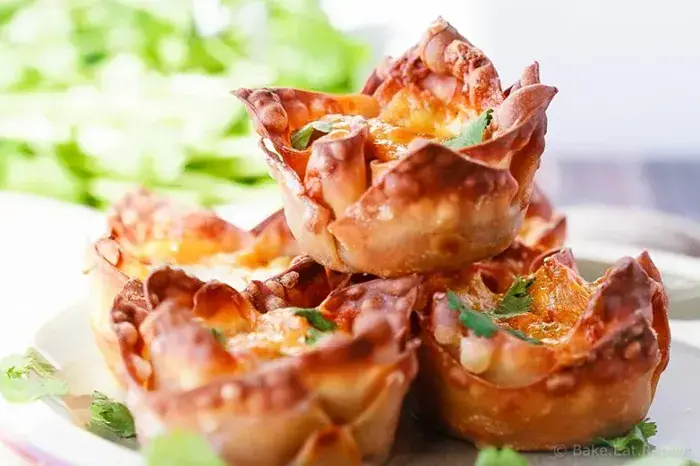Crispy golden wonton cups filled with sweet potato, black beans, taco-seasoned vegetables, and melted cheddar cheese, garnished with fresh cilantro.